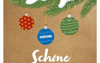 Eine braune Karte, auf der ein mit Schnee bedeckter, grüner Tannenzweig mit Weihnachtskugeln abgebildet ist. Darunter steht "Schöne Weihnachten!"