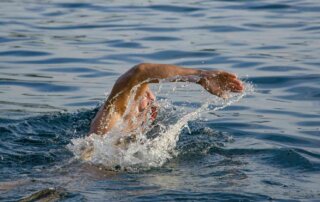 Ein gut trainierter Mann schwimmt in einem Gewässer.