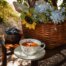Auf einem Stuhl im Garten steht ein Korb mit Blumen, eine Schale mit Blaubeeren und eine Teetasse.