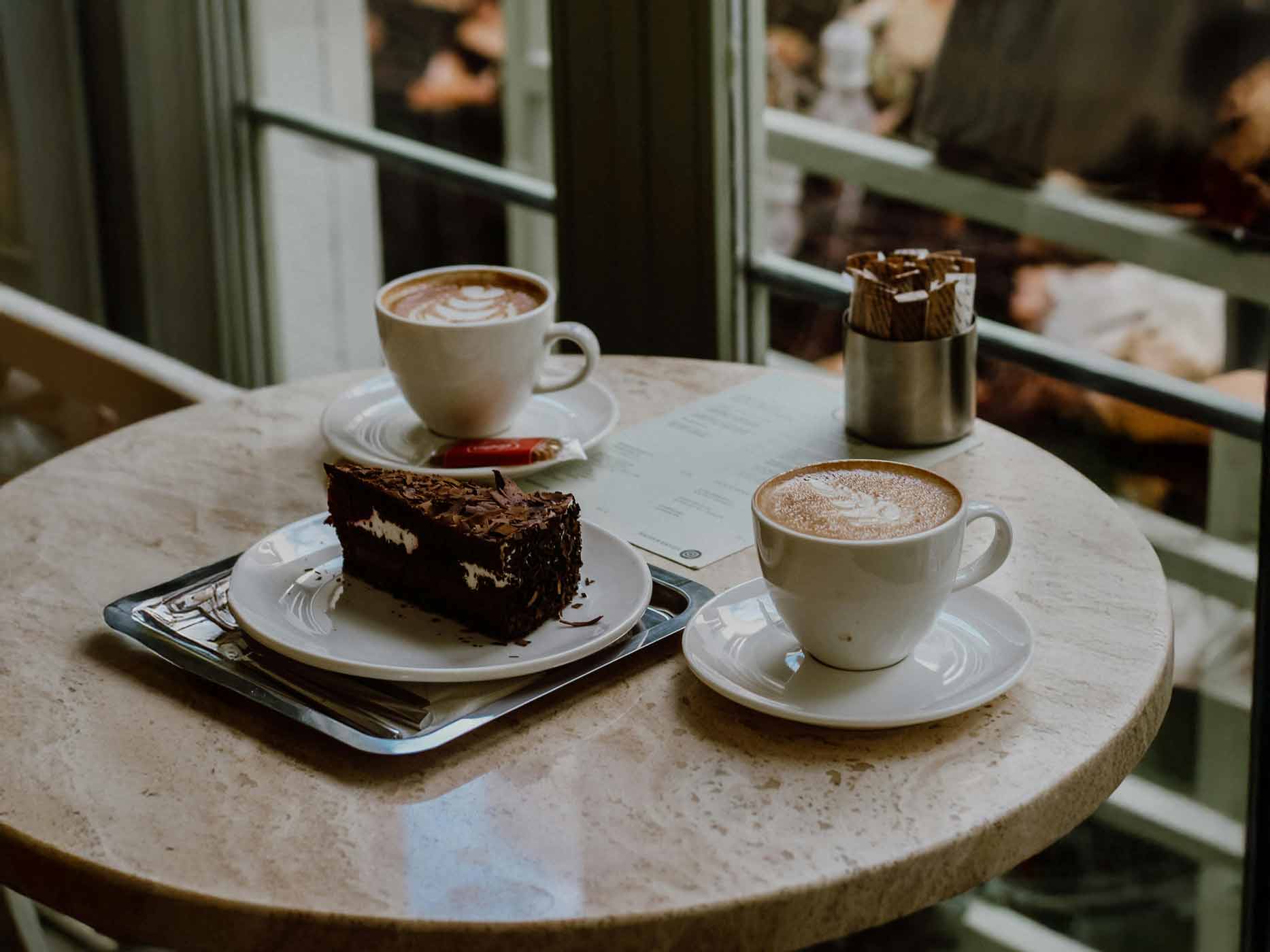 Hildesheimer Herbst Café Zwei Cappuccini stehen hergerichtet mit einem Stück Schokoladenkuchen auf dem Tisch